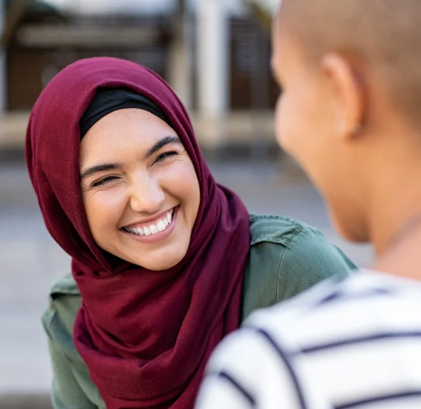 Portrait of cheerful woman in hijab smiling while talking to friend.