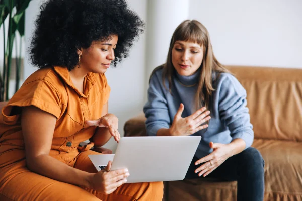 Two young women having a discussion while looking at a laptop screen